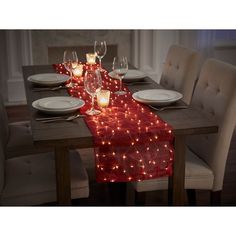 the table is set with white plates and wine glasses on it, along with red lights