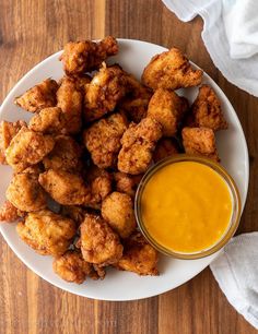 a white plate topped with chicken nuggies next to a bowl of dipping sauce