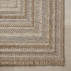 an area rug with braiding on the side and fringes in the middle, against a beige wall