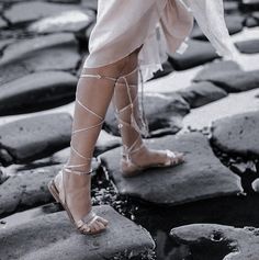 a woman is standing on rocks with her feet in the water and wearing high heels