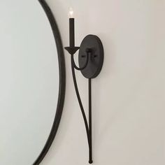 a candle is lit on the wall next to a mirror with a curved black frame