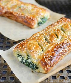 two pieces of bread with spinach and cheese on them sitting on wax paper next to each other