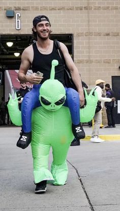 a man is carrying an inflatable alien while walking down the street with other people