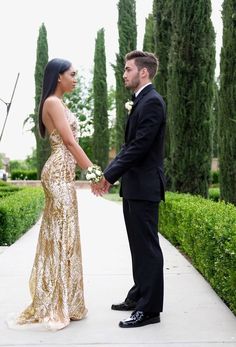 a man and woman standing next to each other in front of some bushes holding hands