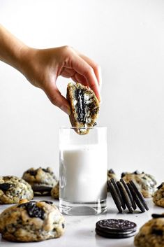 a hand holding a cookie over a glass of milk with cookies and oreos around it