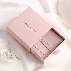 the pink box is next to two earrings on a white cloth with flowers in it