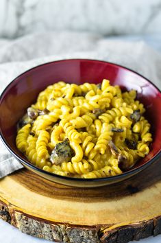 a red bowl filled with macaroni and cheese on top of a wooden board