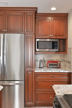 a stainless steel refrigerator and microwave in a kitchen with wooden cabinets, granite counter tops