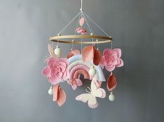 a mobile with pink flowers and butterflies hanging from it's centerpiece, against a gray wall