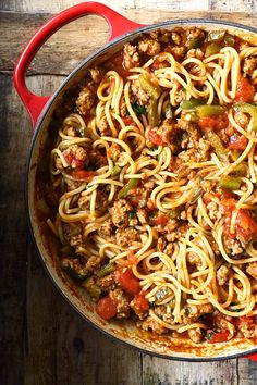 a large pot filled with spaghetti and meat on top of a wooden table next to a red spatula