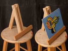 two wooden stools with paintings on them sitting side by side in front of a black backdrop