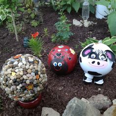 three garden ornaments sitting in the dirt near some rocks and plants with eyes painted on them