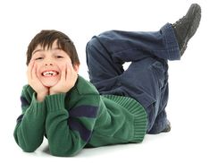 a young boy laying on the ground with his hands under his face and smiling at the camera