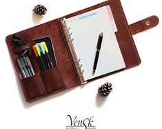 an open notebook with pens, pencils and pine cones