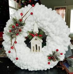 a white wreath with a church and pine cones on it, surrounded by red berries