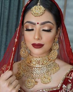 a woman in a red and gold bridal outfit with jewelry on her head, looking down