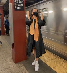 a woman wearing a face mask standing next to a subway platform with her hands on her head