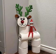 a elf is standing on top of a toilet paper roll reindeer figure next to a wall