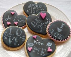 four decorated cookies on a white plate with writing and hearts in the shape of heart