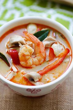 a bowl of soup with shrimp, mushrooms and peppers in it sitting on a table