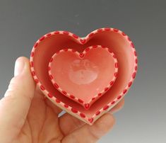 a hand holding a heart shaped bowl in the shape of a heart with red polka dots