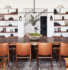 a dining room table with leather chairs and a bowl on top of it in front of shelves