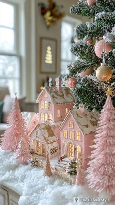 a christmas tree with pink and gold decorations in front of a house on snow covered ground