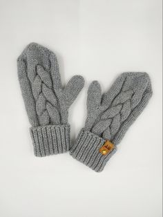 two gray knitted mittens sitting next to each other on a white table top