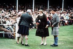 two men in kilts are shaking hands with an older woman wearing a tartan dress