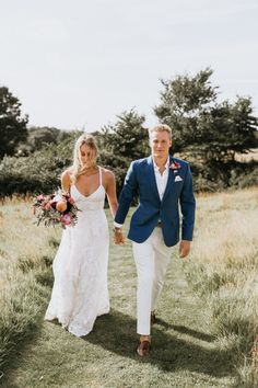 a bride and groom walking through the grass