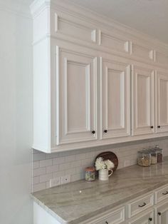 a kitchen with white cabinets and marble counter tops