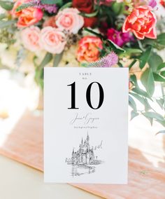 a table number with flowers and greenery in the background for an elegant wedding reception