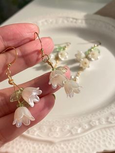 a person is holding two flower earrings in their left hand and another one with pearls on it