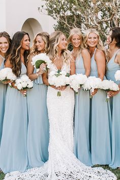 a group of women standing next to each other in front of a white building holding bouquets