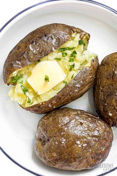 three baked potatoes on a plate with butter and parsley