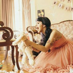 a woman in a pink dress holding a white teddy bear while sitting on the floor