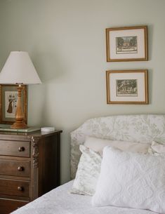 a white bed sitting next to two framed pictures on the side of a bedroom wall