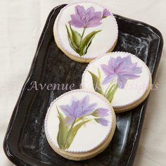 three decorated cookies with flowers on them sitting on a black platter next to a white tablecloth