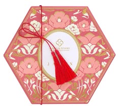 a pink and gold box with a red tassel on it's side, decorated with flowers