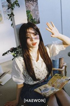 a woman sitting on the floor with her hand up in the air while reading a magazine