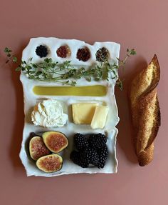 an assortment of cheeses, fruits and bread on a pink plate with sprigs