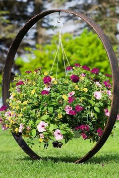 a hanging planter filled with pink and yellow flowers in a circular metal holder on grass