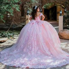 a woman in a pink ball gown standing on a stone walkway with her hands on her hips