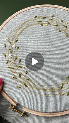 someone is holding up a embroidery project on a hoop with flowers and leaves in it