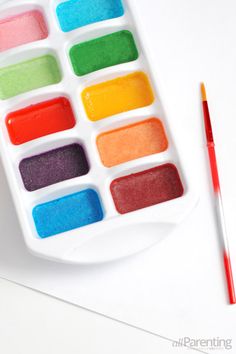 a white tray with different colored paints next to a red brush