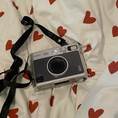 an old camera is laying on a bed with red heart - shaped sheets and a black strap