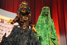 two people in costumes standing on stage with red curtains behind them and one person wearing green