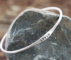 a silver bracelet with the word loved on it sitting on top of a large rock