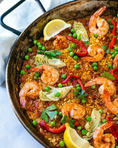 a skillet filled with shrimp, rice and peas on top of a white table