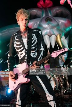 a man in skeleton clothing playing guitar on stage at a concert with an animal sculpture behind him